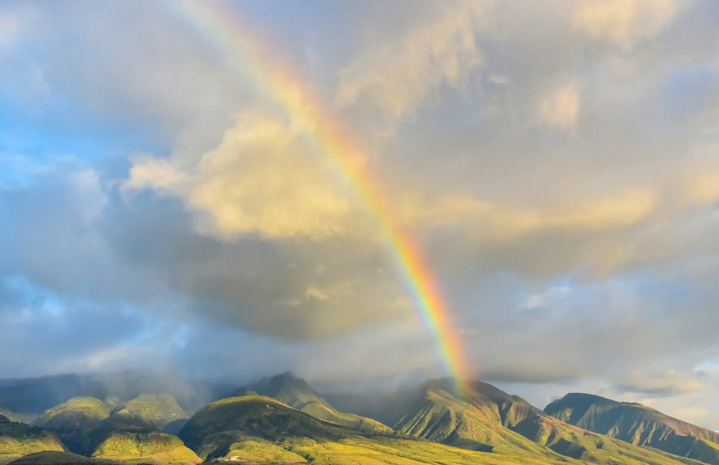 A rainbow arcing over green mountain ridges after rain in Hawaiʻi