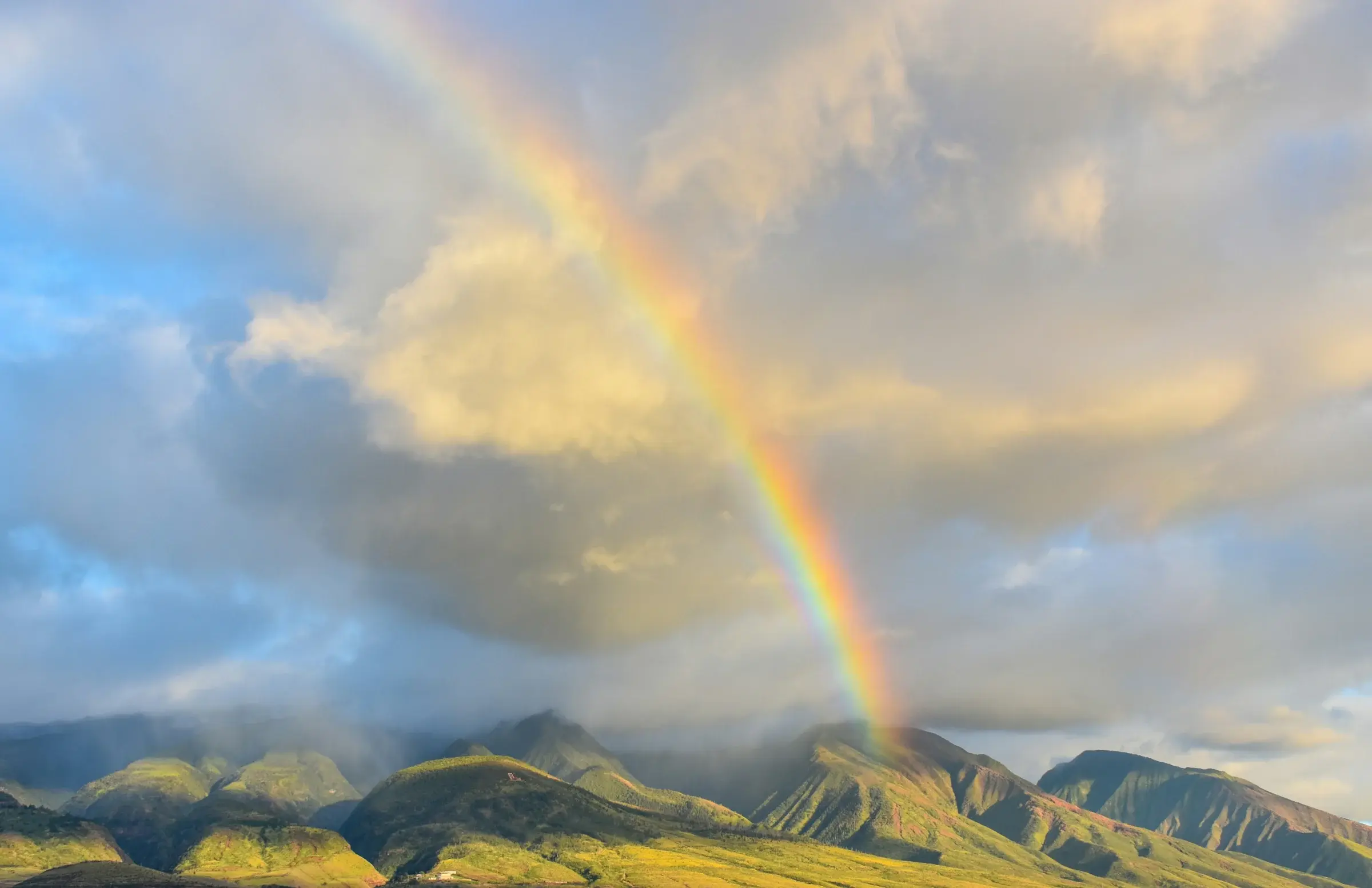 A rainbow arcing over green mountain ridges after rain in Hawaiʻi
