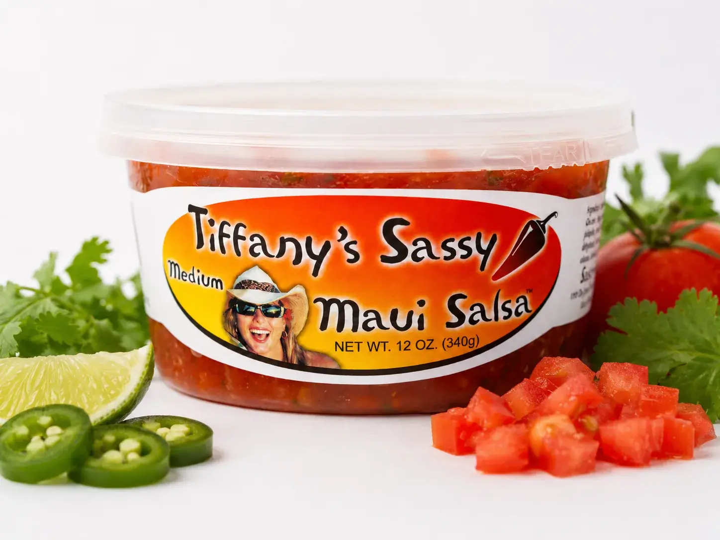 A 12 oz tub of Tiffany's Sassy Maui Salsa styled with fresh produce
