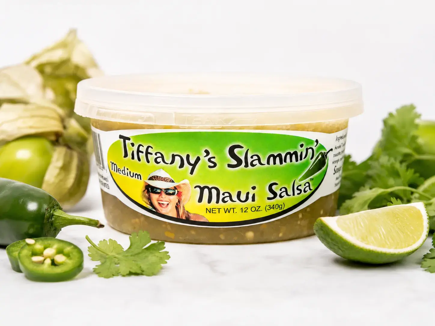 A 12 oz tub of Tiffany's Slammin' Maui Salsa styled with fresh produce