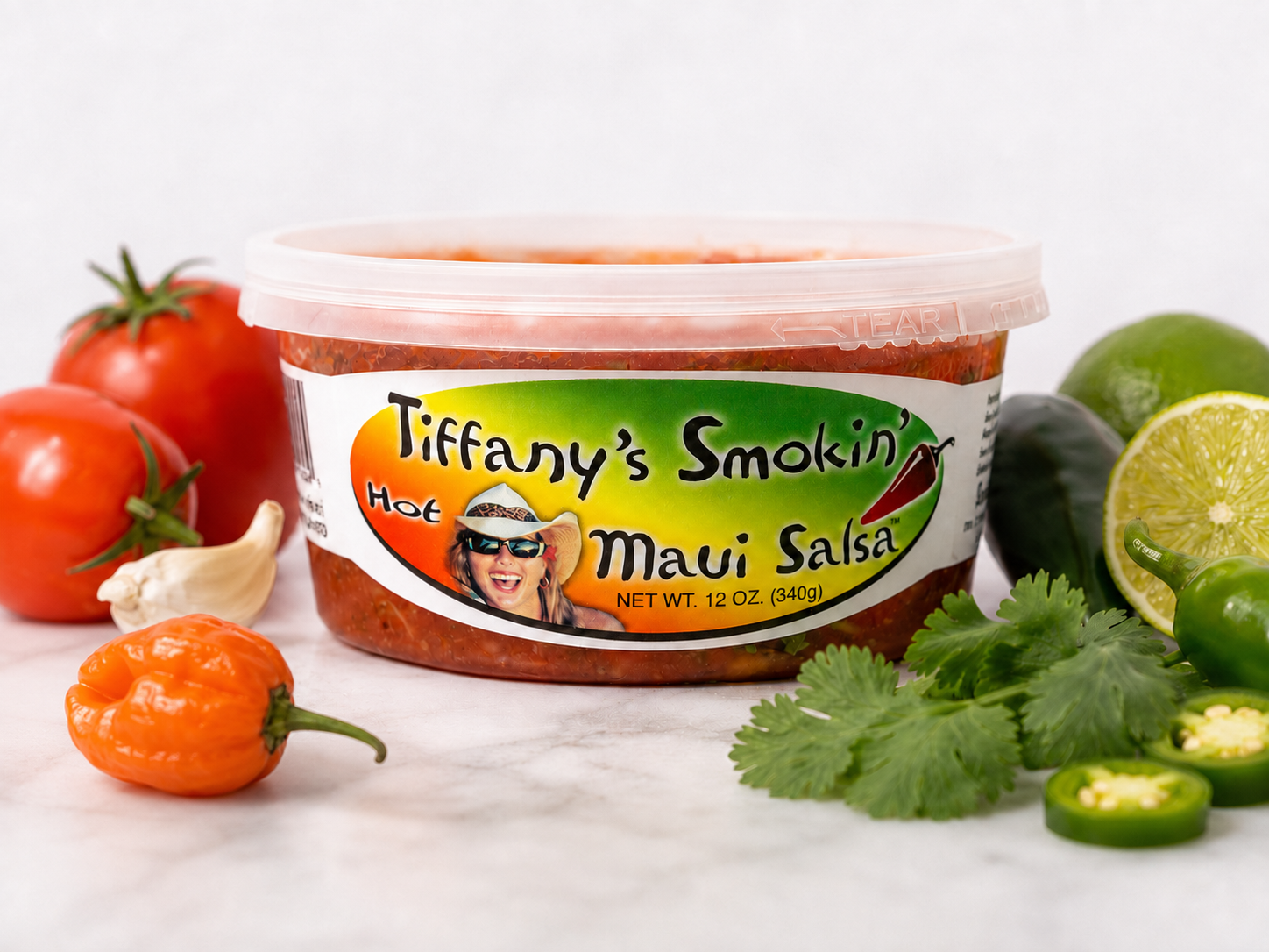 A 12 oz tub of Tiffany's Smokin' Maui Salsa styled with fresh produce
